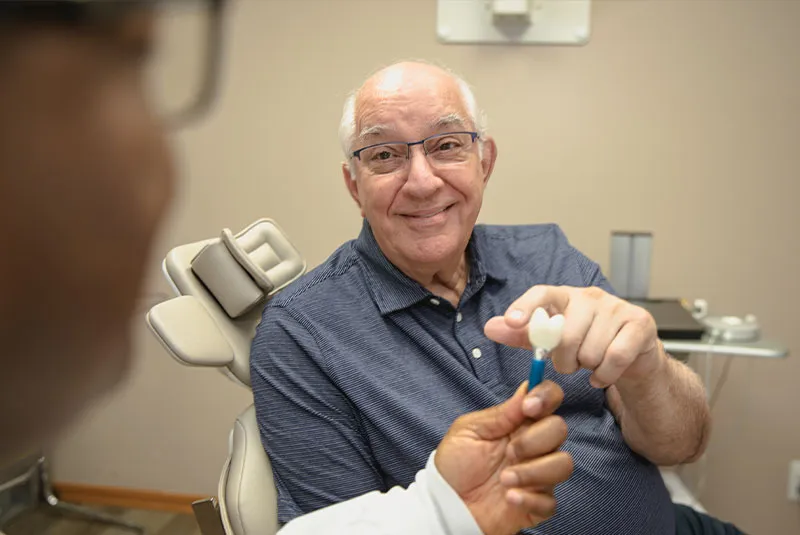 Dr. O with male dental patient looking at dental implant examples.